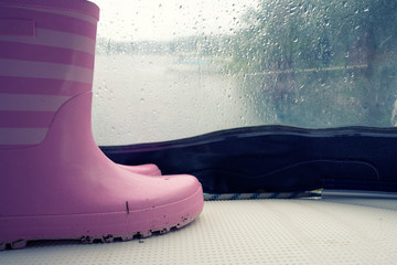 Plastic rain boots pink color on white floor and raining outside