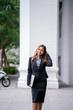 © Danon - Portrait of a beautiful, young and attractive Southeast Asian woman in a business suit walking in a city in Asia during the day with her laptop computer. She is smiling confidently.