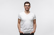 © Damir Khabirov - Handsome smiling man in white t-shirt and trendy eyeglasses, standing with hands in pockets,  isolated on gray background