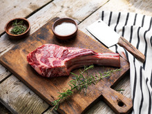 Raw Fresh Angus Meat Tomahawk On A Wooden Cutting Board With Rosemary, Salt And Butcher's Knife