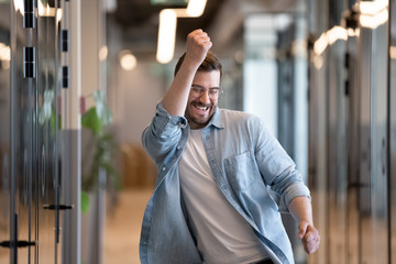 Wall Mural - Ecstatic male winner dancing in office hallway laughing celebrating success