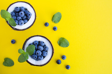Wall Mural - Blueberries  in half coconut on the yellow  background.Top view. Copy space.