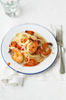 © The Picture Pantry - Spaghetti with pan seared prawns, oven roasted tomatoes and parmesan, on an enamel plate with a fork, glass and linen. Light background.