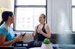 © AYAimages - Chinese woman physiotherapist talking to a mid-adult caucasian female patient and taking notes on a tablet during a fitness evaluation consultation