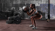 Muscular Woman Doing Intense Squats With Medicine Ball In Gym.