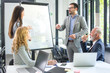 © Bojan - Entrepreneurs discussing business plans on a flip chart board in meeting room. Group of business people having meeting in office.