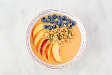Wall Mural - Healthy peach smoothie bowl with blueberries and granola. Top view on a bright background.