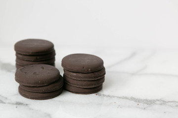 Wall Mural - Stack of thin mints cookies on white marble background, chocolate mint thin round cookies