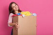 canvas print picture - Portrait of cheerful tender female holding carton box in arms, taking items of clothes, being volunteer, having kind heart, smiling sincerely, looking directly at camera. Copyspace for advertisement.