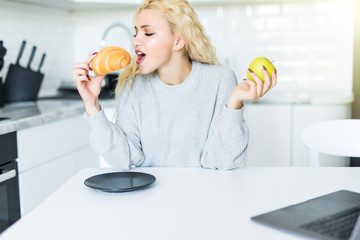 Young blonde girl with croissants on a plate, apples on a white kitchen table in the kitchen