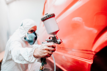 industry details - mechanic engineer using spray gun and painting a red car