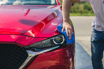 Car detailing - the man holds the microfiber in hand and polishes the car. Selective focus. Car detailing series : Worker cleaning red car. 