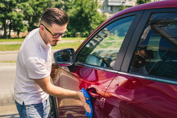 Wall Mural - Car detailing - the man holds the microfiber in hand and polishes the car. Selective focus. Car detailing series : Worker cleaning red car. 