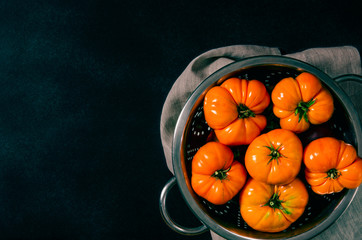 Washed various tomatoes in a colander on a black background