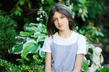 Beautiful smiling teenage girl in blue blouse, against green of summer park.