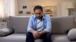 © motortion - Sad lonely man aggressively looking into camera sitting on sofa at home, problem