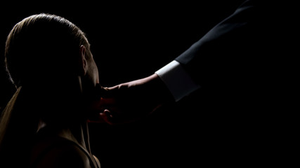 male hand touching young female face against dark background, human trafficking