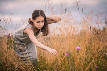 evening, a girl in a field reaches for a flower