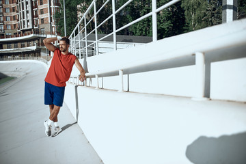 Sporty man standing near fence, resting after training in city