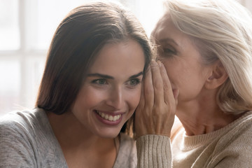  Middle aged mother whispering secret to grown up daughter