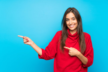 Wall Mural - Young woman with red sweater over isolated blue background pointing finger to the side