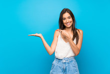 Young Woman Over Isolated Blue Background Holding Copyspace Imaginary On The Palm To Insert An Ad