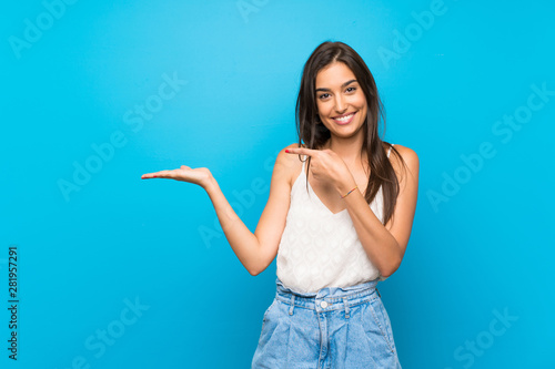 Cuadros en Lienzo Young woman over isolated blue background holding copyspace imaginary on the pal