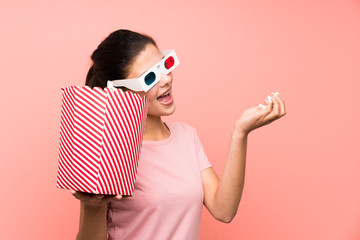 Teenager girl over isolated pink wall eating popcorns with 3d glasses