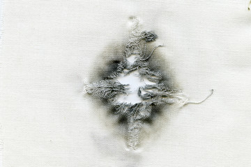 Bullet hole on a white cloth when shot at point-blank range from a 45-gauge weapon, abstract background.