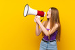 © luismolinero - Young woman over isolated yellow background shouting through a megaphone