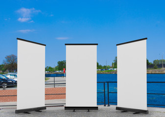 Wall Mural - 3D rendering of blank vertical rollup (empty billboard advertisement) with city background. Empty mockup template