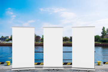 Wall Mural - 3D rendering of blank vertical rollup (empty billboard advertisement) with city background. Empty mockup template