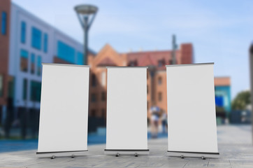 Wall Mural - 3D rendering of blank vertical rollup (empty billboard advertisement) with city background. Empty mockup template