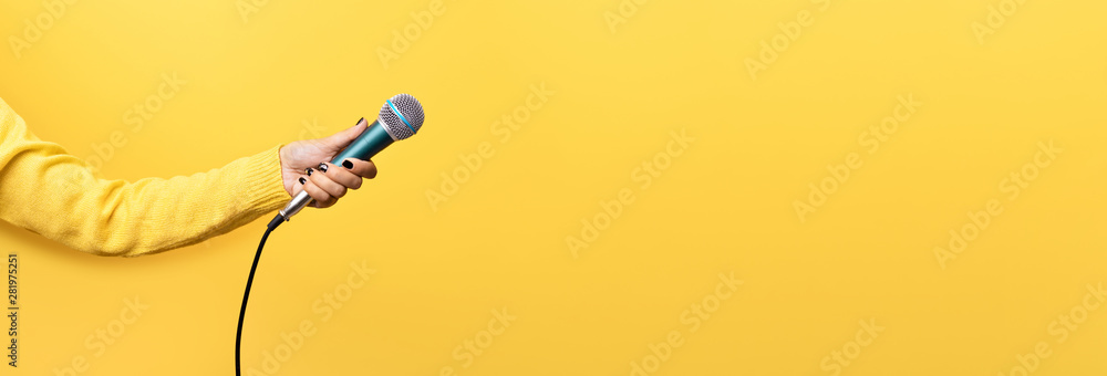 hand holding microphone over yellow background, panoramic mock up image - obrazy, fototapety, plakaty 