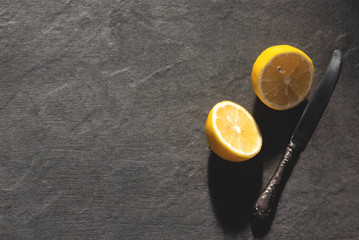 Sliced fresh lemon and a kitchen knife on a black stone cutting board background with copy space.