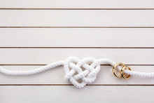 Heart Shaped Rope And A Double Gold Ring On White Wooden Background