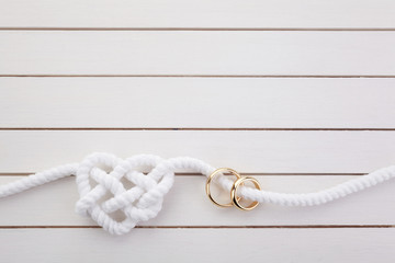 Wall Mural - Heart shaped rope and a double gold ring on white wooden background