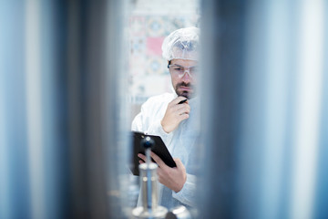 Technologist in protective white suit working in food processing industry plant being concentrated and controlling production.