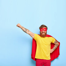 Brave Cheerful Man Hero Ready To Fly, Can Sacrifice Own Life To Help Other, Has Extraordinary Ability, Wears Red Cape And Mask, Yellow T Shirt, Isolated On Blue Background, Performs Act Of Kindness