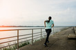 © ParinPIX - Young woman running on the street with a view of the river in the morning.