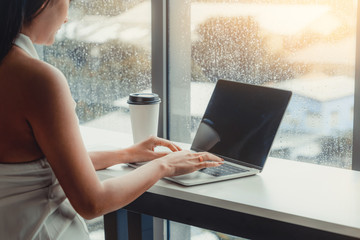 Young business woman using laptop computer while sitting at cafe table next to office windows.