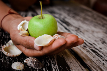 Close up of hand holding green apple in background of wooden table and shell.