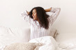 © Anatoliy Karlyuk - Attractive young African American female in striped silk pajamas waking up on weekend morning, stretching body, raising hands, having joyful facial expression, sitting on bed, ready to begin new day