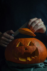 Man looking into Jack's lantern orange pumpkin for traditional autumn holiday Halloween. One hand is holding pumpkin cap and other is holding knife