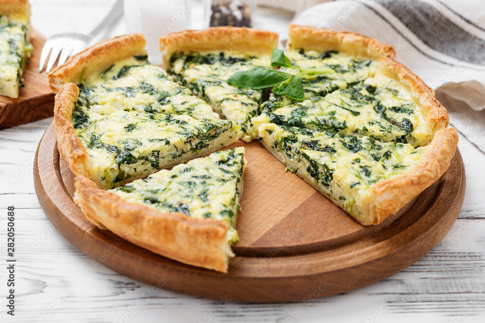 Vegetarian spinach pie or tart with feta cheese on white wooden background. - obrazy, fototapety, plakaty 