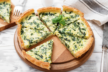 Vegetarian spinach pie or tart with feta cheese on white wooden background.