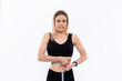 © ianachyrva - Young blond woman in a black sportswear with smart watches is shocked checking her waist with tape measure after workout standing over white background.