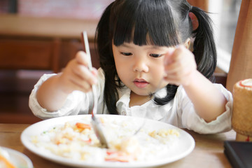 Wall Mural - Asian child cute or kid girl enjoy eating shrimp fried rice delicious food with hungry on wood table and white dish for breakfast or lunch and dinner in the cafe restaurant with holding spoon and fork