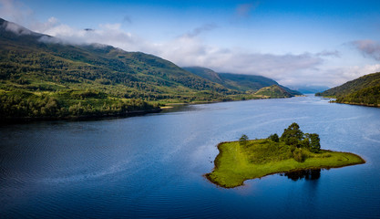 Wall Mural - aerial view of loch leven near kinlochleven and glen coe in the argyll region of the highlands of scotland with a green island in the foreground and calm blue waters with misty mountains