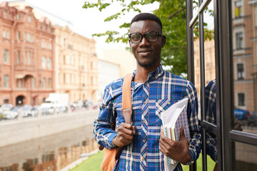 Wall Mural - Waist up portrait of smiling African-American student posing outdoors in college campus and looking at camera, copy space